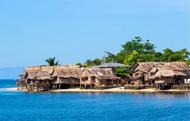 Traditional thatched roof stilt houses in a tropical coastal village along blue ocean waters.
