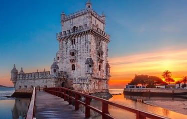 The historic Belem Tower in Lisbon at sunset with a wooden walkway over the Tagus River.