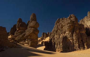 Tall volcanic rock formations and sand dunes under a clear blue sky in the Sahara Desert, Chad