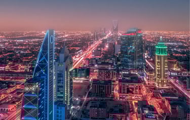 Aerial night view of Riyadh skyline featuring illuminated skyscrapers and city traffic lights in Saudi Arabia.