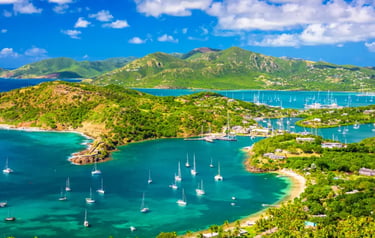 Aerial view of sailboats anchored in the turquoise waters of English Harbour, Antigua, surrounded by lush green hills.