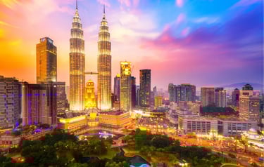 Petronas Twin Towers and Kuala Lumpur city skyline illuminated at sunset with vibrant purple and orange clouds.