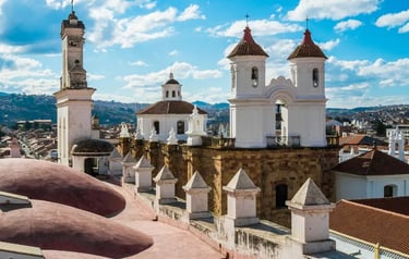 Historic white church towers and rooftop views of Sucre, Bolivia, under a blue sky.