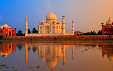 The Taj Mahal in Agra reflected in the Yamuna River during a golden hour sunset.