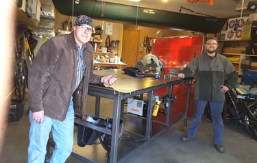 Two Welders standing by a welding table