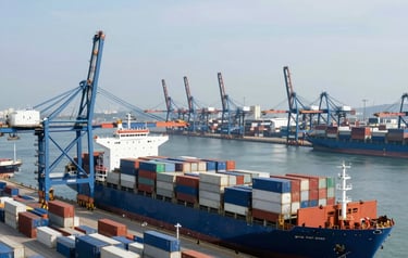A high-angle professional photograph of a bustling international port with cargo ships and containers, symbolizing global commerce, in the daylight with a clear sky, featuring Medium Blue and Light Blue tones, International / Global style.