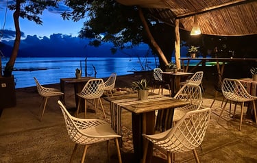 Cozy outdoor beachfront restaurant seating with white modern chairs at twilight.