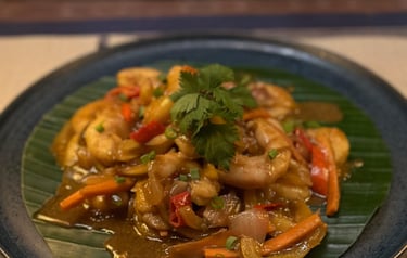 Spicy Thai shrimp stir fry with vegetables and cilantro on a banana leaf plate.
