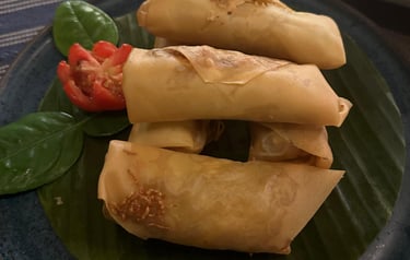 Crispy golden fried spring rolls served on a banana leaf with tomato and herb garnish.