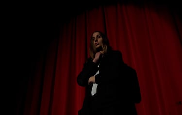 Aodh, played by Finn Rooney, standing in front of a red velvet curtain in a theatre