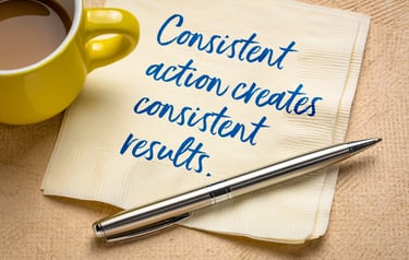 consistent action creats consistent results handwritten on a napkin amd a pen near a cup of coffee