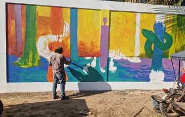 Artist painting a colorful mural on a large outdoor wall featuring vibrant forest-inspired patterns.