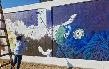 Artist uses a paint roller on a ladder to create a vibrant mural at Centro Recreacional Mokanranko 