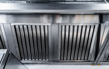 A commercial stainless steel kitchen exhaust hood with parallel slats for air filtration.