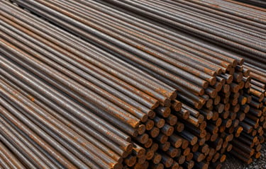 Close overhead shot of bundled TMT steel rods stacked in a storage yard, site daylight, rust-free ribbed surface texture visible, no people