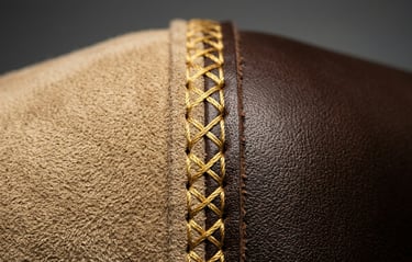 Close-up of intricate gold cross-stitching on premium brown leather and tan suede fabric.