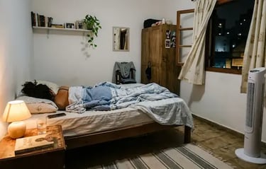 A person sleeping in a cozy bedroom with a warm bedside lamp and a modern tower fan.