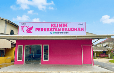Pink storefront of Klinik Perubatan Raudah medical clinic with large signage under a blue sky.