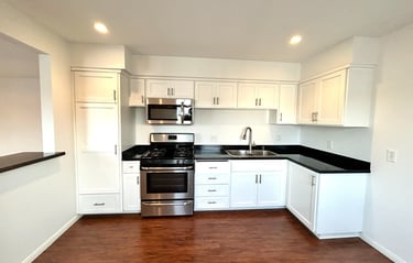 A modern kitchen with white cabinetry, black countertops, and stainless steel appliances