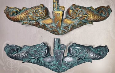 Pic of a gold Submarine Warfare Insignia Officers dolphins over a silver Enlisted dolphin sculpture. 