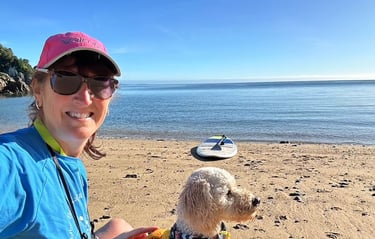 picture of a woman and a dog on a beach with a paddle board