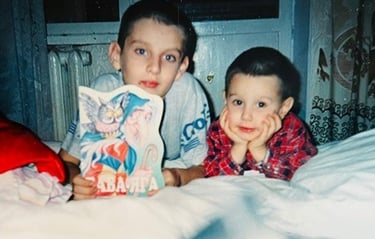 Two young brothers at bedtime: the elder holds a picture book, and the younger smiles at the camera.