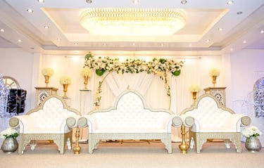 inside wedding venue, regal white chairs, flowers and draping background, large chandelier in centre