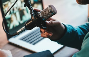 A person recording a podcast using a professional condenser microphone and a laptop computer.