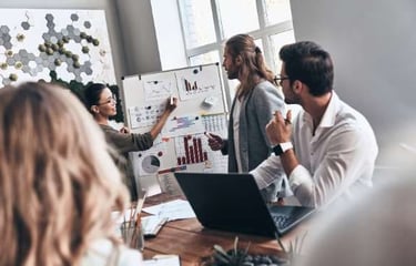 a group of people in a meeting room with a man pointing at a boardroom
