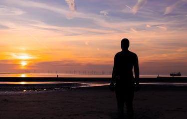 Silhouette of Antony Gormley's Another Place iron man statue on Crosby Beach during a golden sunset.