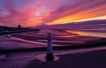 Aerial view of Perch Rock Lighthouse on New Brighton beach at sunset with purple sky.