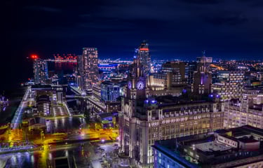 Night aerial view of Liverpool city skyline featuring the Royal Liver Building and illuminated waterfront docks.