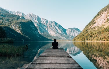a person sitting on a dock with a mountain in the background