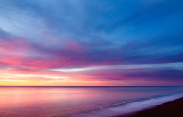 a sunset on a beach with a lighthouse in the background
