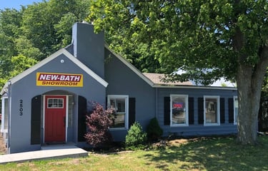 Front view of the New Bath Elite showroom in Perrysburg, Ohio, featuring a gray building with a red door, bright yellow logo 