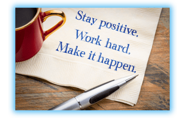 Napkin with the words, "Stay positive. Work Hard. Make it happen"  on table with a cup of coffee and a pen