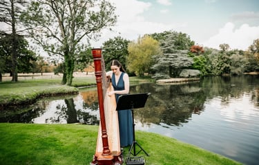 Harpist performing by a lakeside during an outdoor wedding.