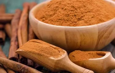 A wooden bowl and scoops filled with ground cinnamon powder next to cinnamon sticks on a rustic table.