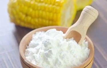 White cornstarch powder in a wooden bowl with a scoop and yellow corn on the cob.