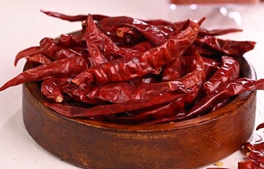 A wooden bowl filled with whole dried red chili peppers for cooking spicy food.