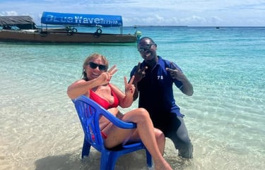 Smiling tourist sitting on a chair at Nakupenda Beach, Zanzibar, accompanied by a friendly local tour guide by the clear wate