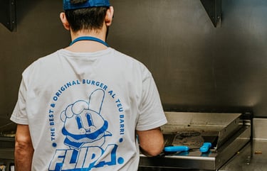 Cuiner de Flipa a la cuina amb samarreta de la marca mentre prepara burgers a la planxa