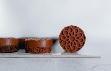 Miniature round brownie cakes with intricate geometric floral designs on a white surface.