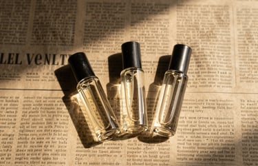 Overhead flat-lay of three small glass perfume vials resting on a vintage newspaper, sharp studio shadows, warm golden light