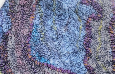 A textured piece of handmade felt art featuring blue, purple, and gray wool fibers in a bubbly pattern.