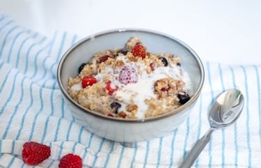A bowl of healthy oatmeal porridge topped with fresh raspberries, blueberries, and a drizzle of milk.