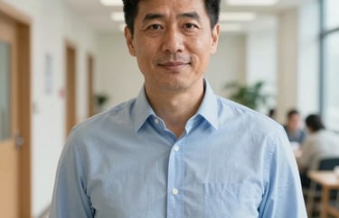 A professional portrait of a man in his late 40s wearing a light blue button-down shirt, looking helpful and friendly, in a bright community center hallway.