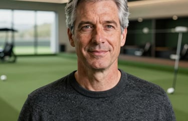 A professional headshot of an approachable man in his 50s with silver-gray hair, wearing a professional charcoal sweater, set against a clean, modern clubhouse interior.