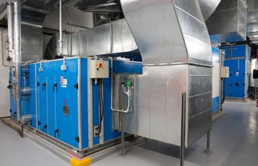 Industrial blue HVAC air handling unit with galvanized steel ductwork in a mechanical plant room.