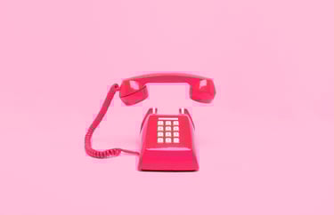 Red desktop, push-button phone with the earpiece hovering over the phone all on a pink background.